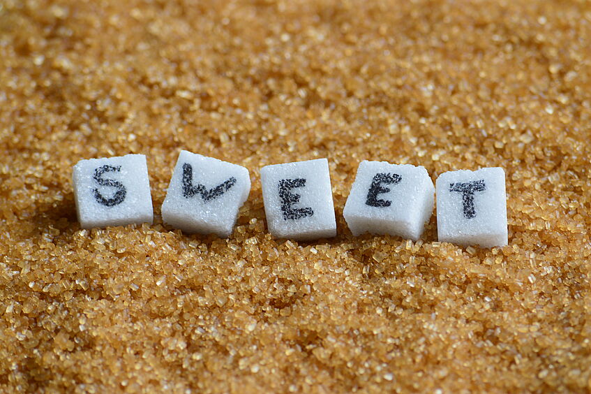 beschriftete Zuckerwürfel auf braunen Zucker mit dem Schriftzug Sweet